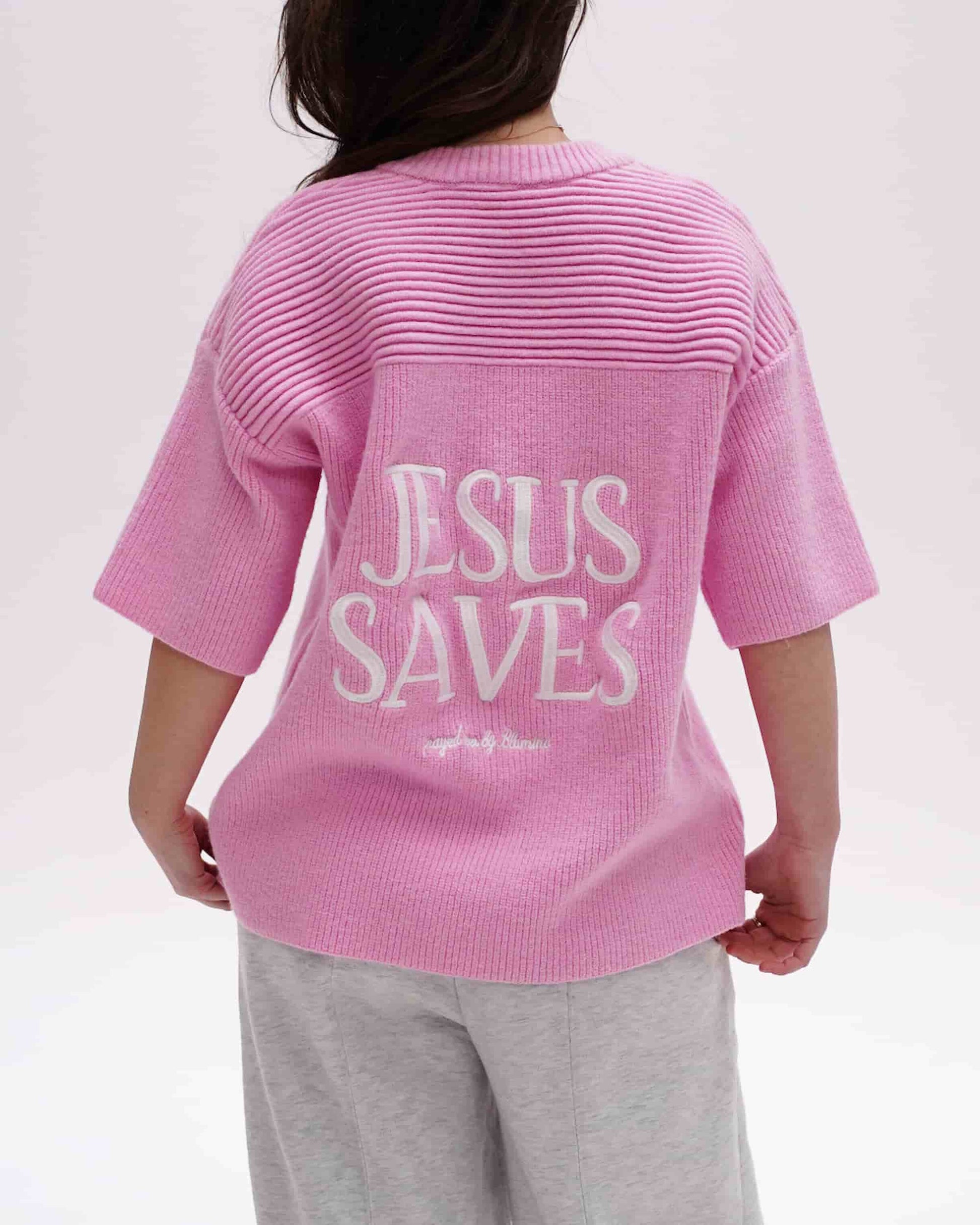 Person wearing a pink shirt with 'Jesus Saves' text on the back against a white background