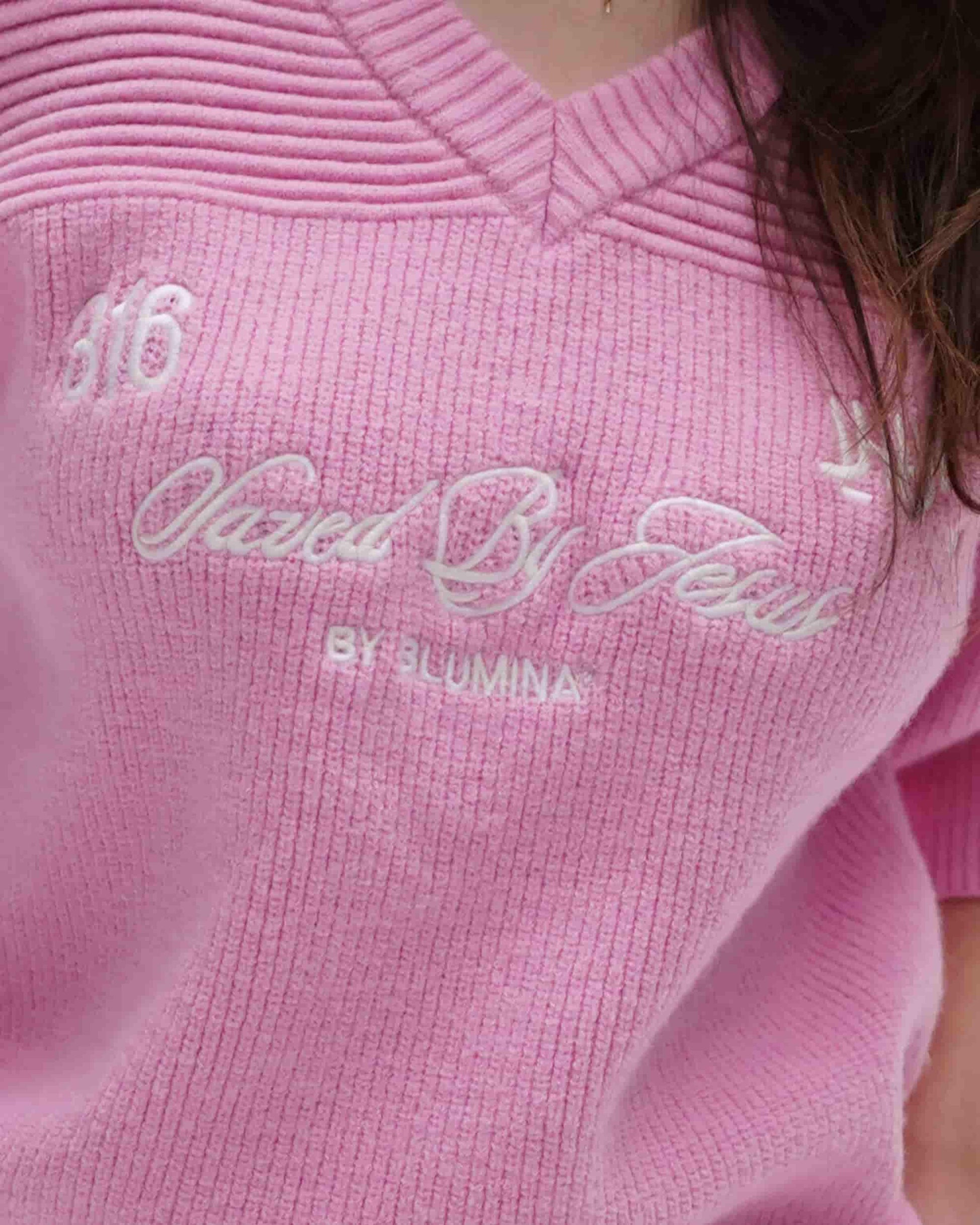 Close-up of a pink sweater with embroidered text and brand name.