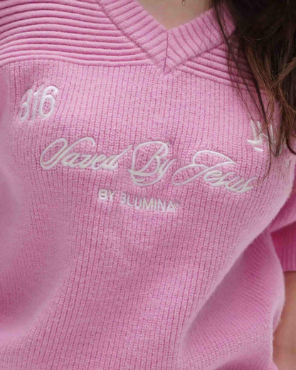 Close-up of a pink sweater with embroidered text and brand name.