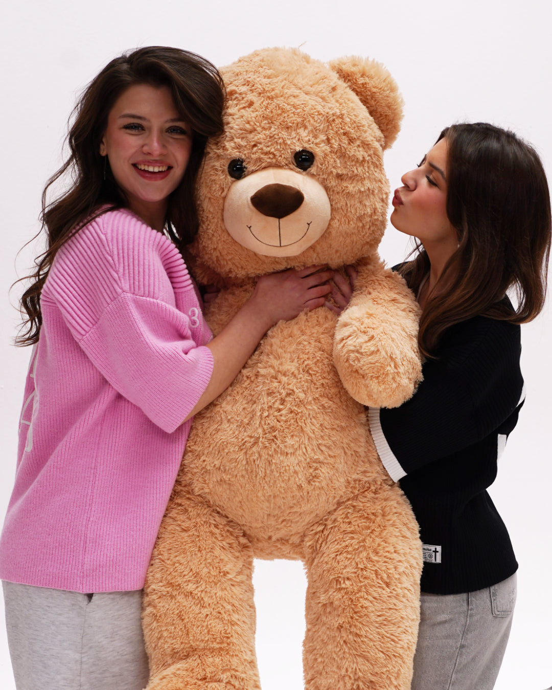 Two people holding a large teddy bear against a white background