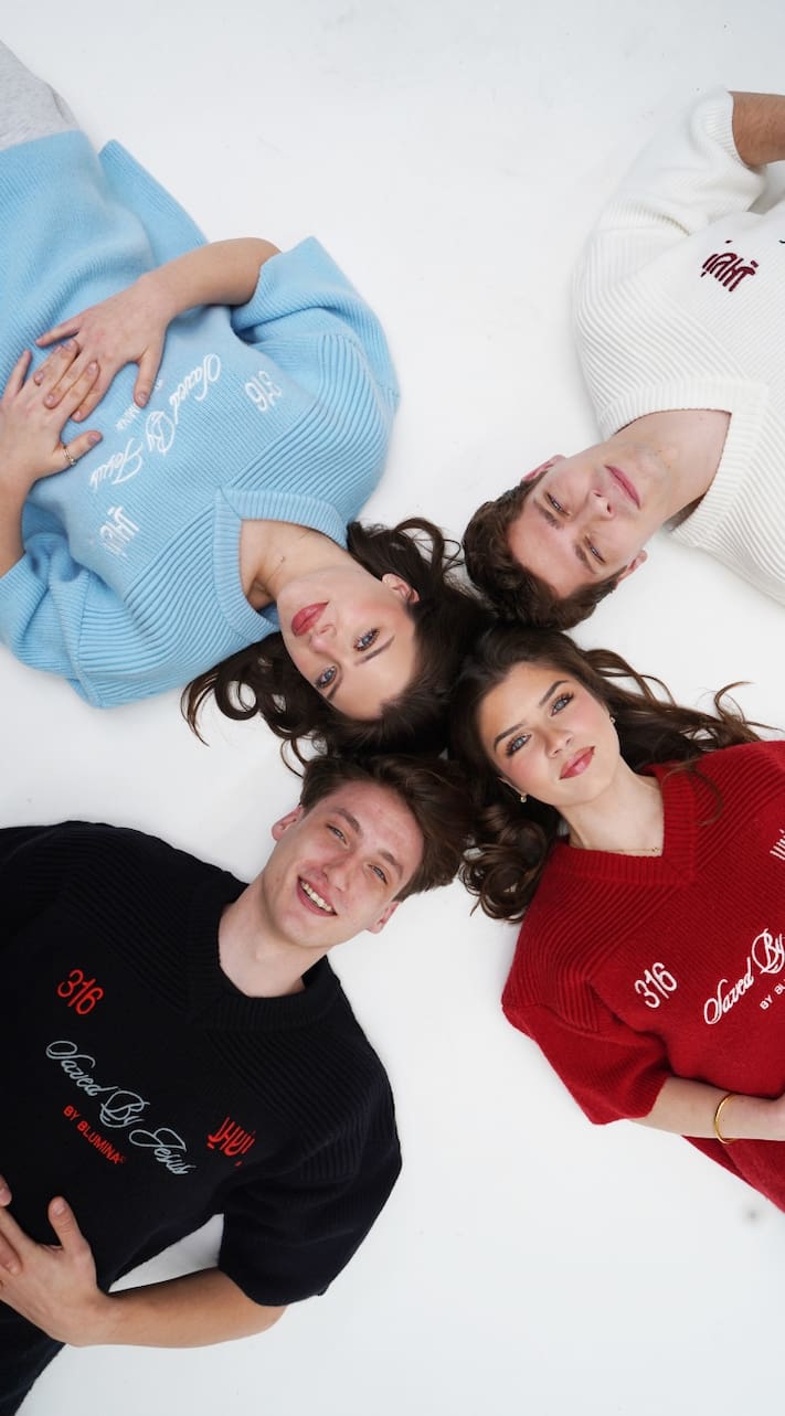 Four people lying on a white surface wearing sweaters with text.