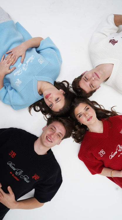 Four people lying on a white surface wearing sweaters with text.